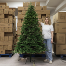 Woman standing next to a decorated Christmas tree in a warehouse setting with stacked boxes.