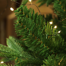 Close-up of a green artificial Christmas tree branch with lights in the background